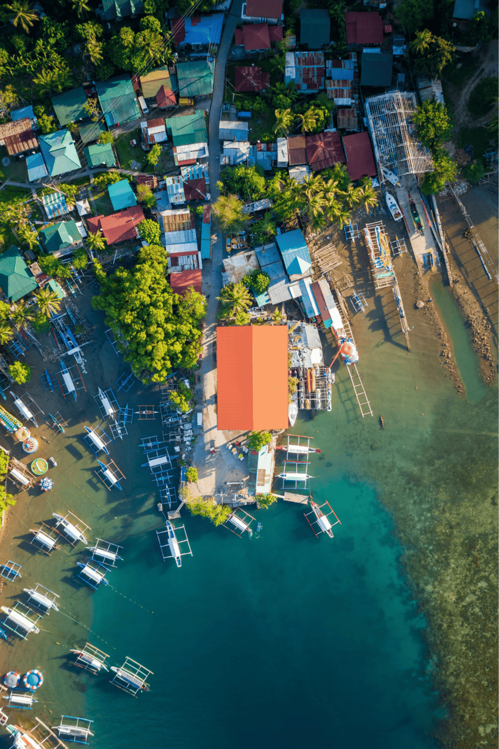 Colorful waterfront village with boats, lush trees, and a central building, perfect for travel and island exploration.