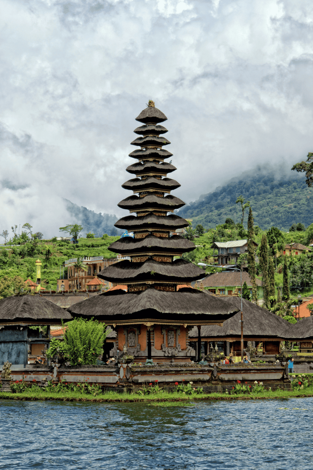 Colorful traditional Balinese pagoda near river in lush green landscape, popular Bali sightseeing spot.
