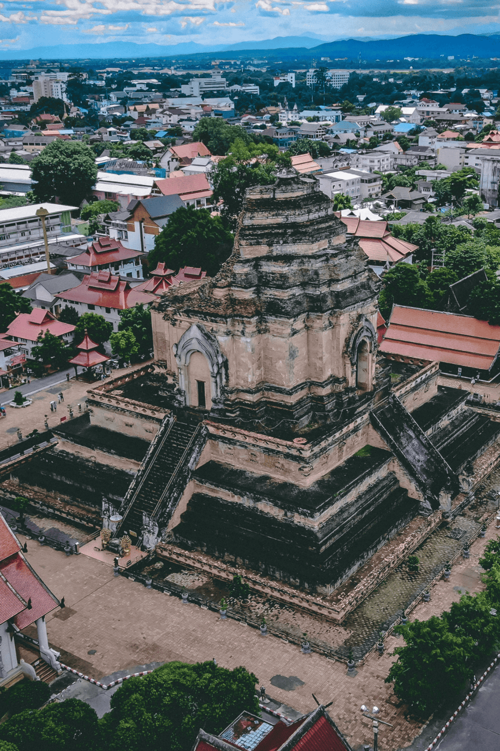 Ancient Buddhist temple in Chiang Mai, Thailand, with cityscape and mountains in background.
