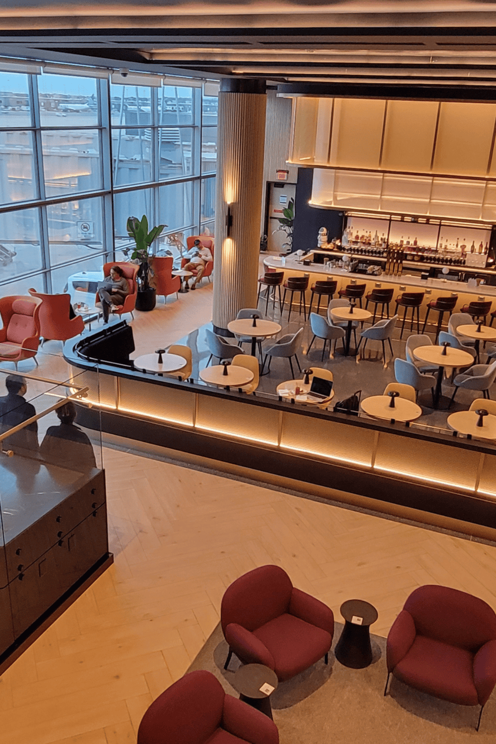 Modern airport lounge with bar, comfortable seating, and large windows overlooking aircraft runway.