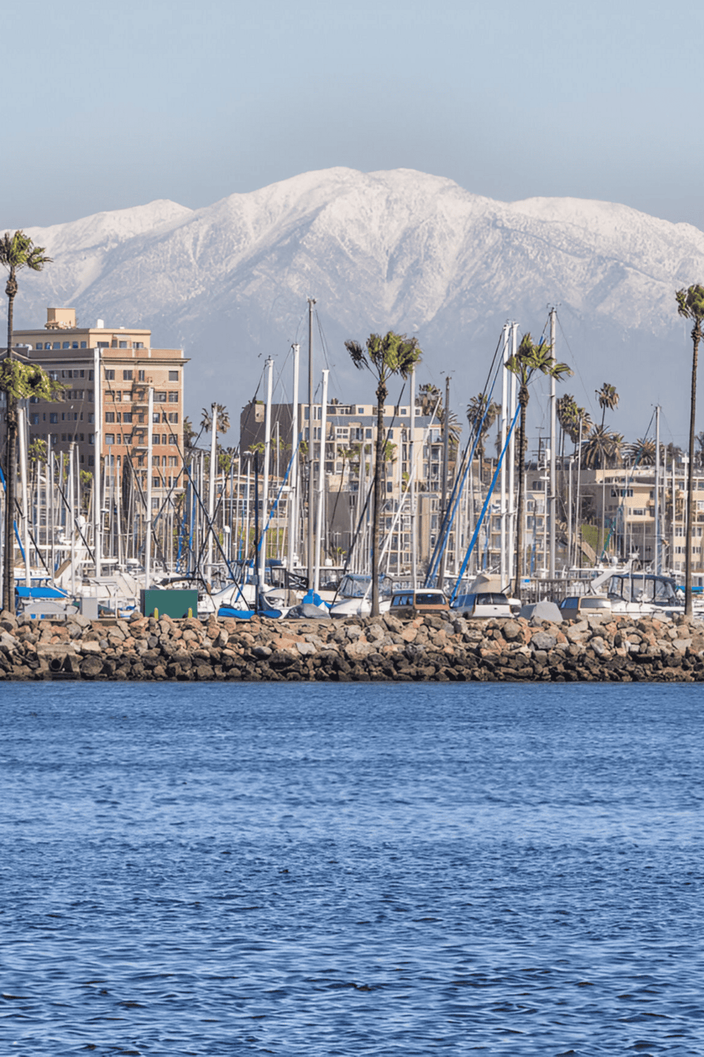 Boats at marina with snow-capped mountains in the background, sunny California waterfront scene.