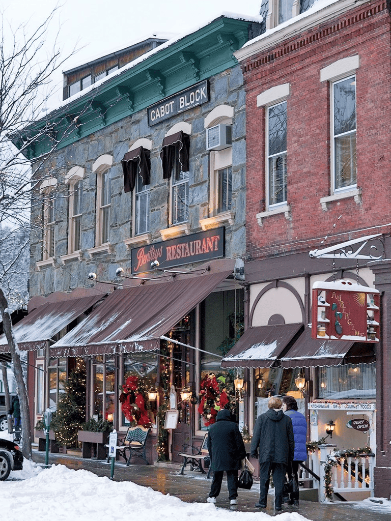 Warm winter scene outside a cozy restaurant on Cabot Block with festive decorations and snow-covered streets.