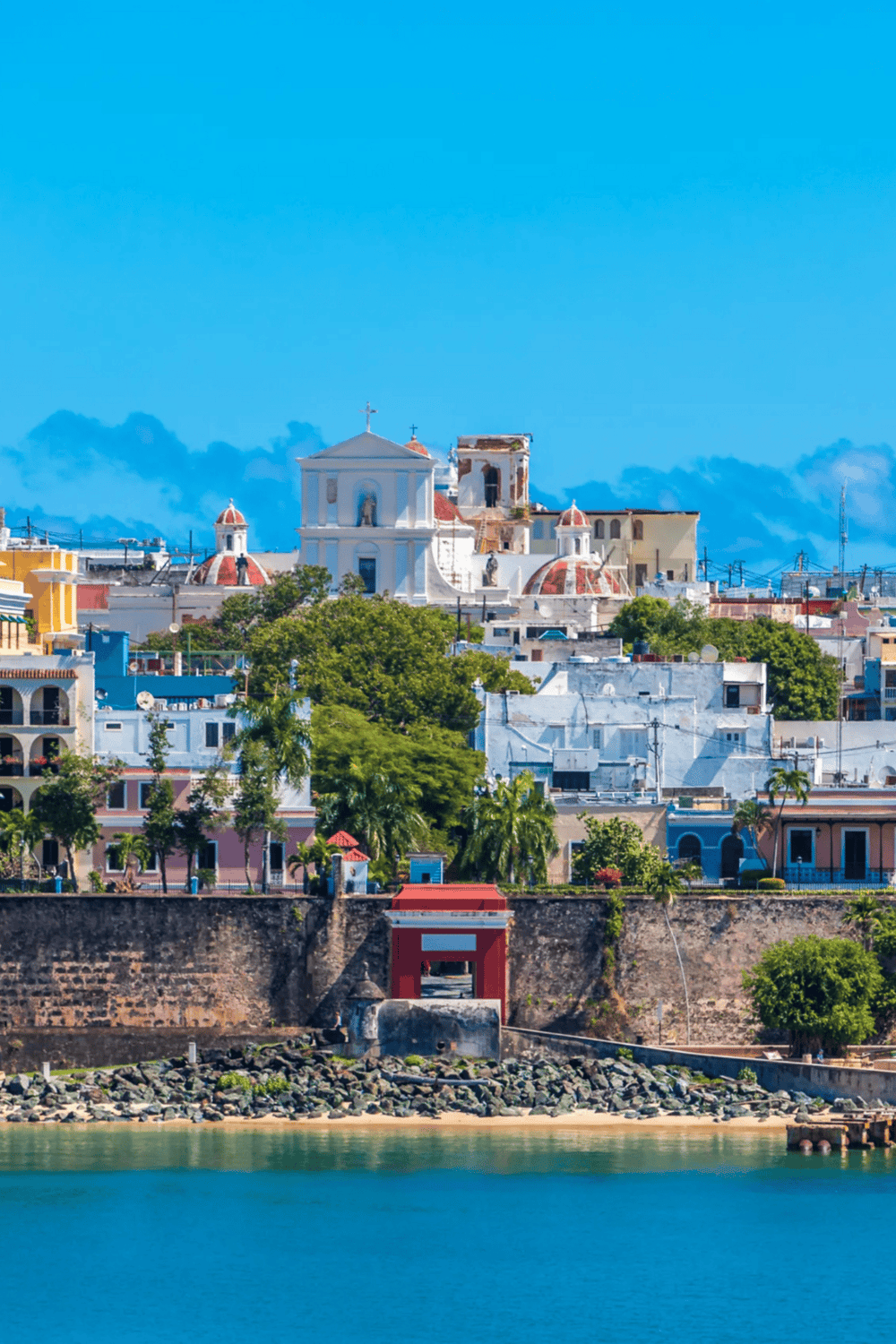 Colorful coastal cityscape of San Juan, Puerto Rico with historic buildings, lush greenery, and vibrant architecture.