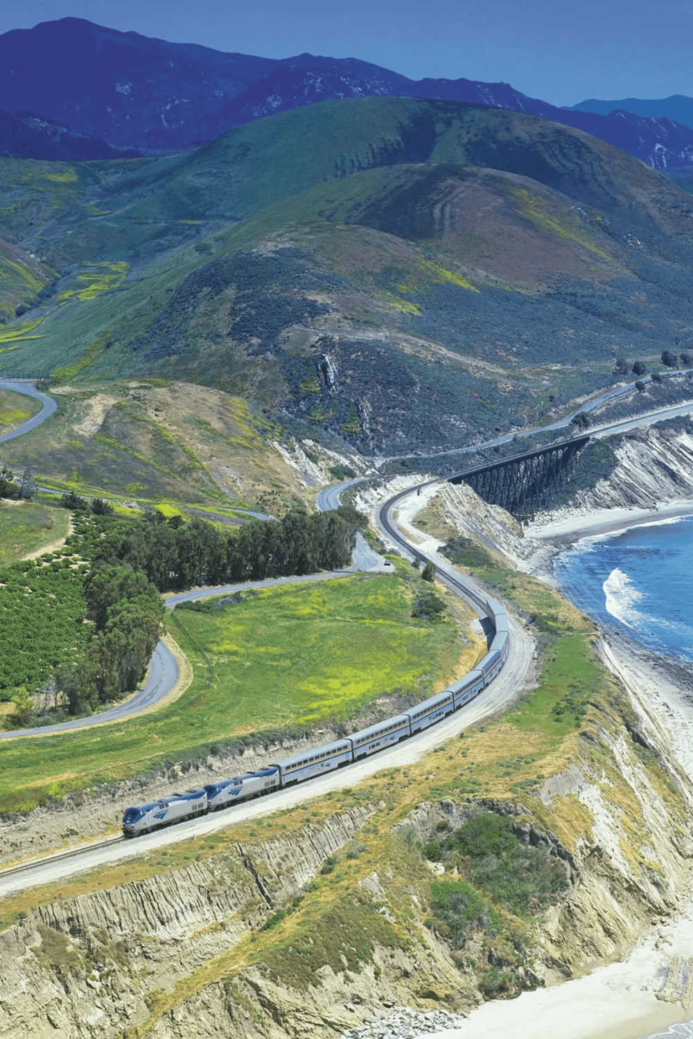 High-speed train traveling along scenic coastal landscape with mountains and ocean views.