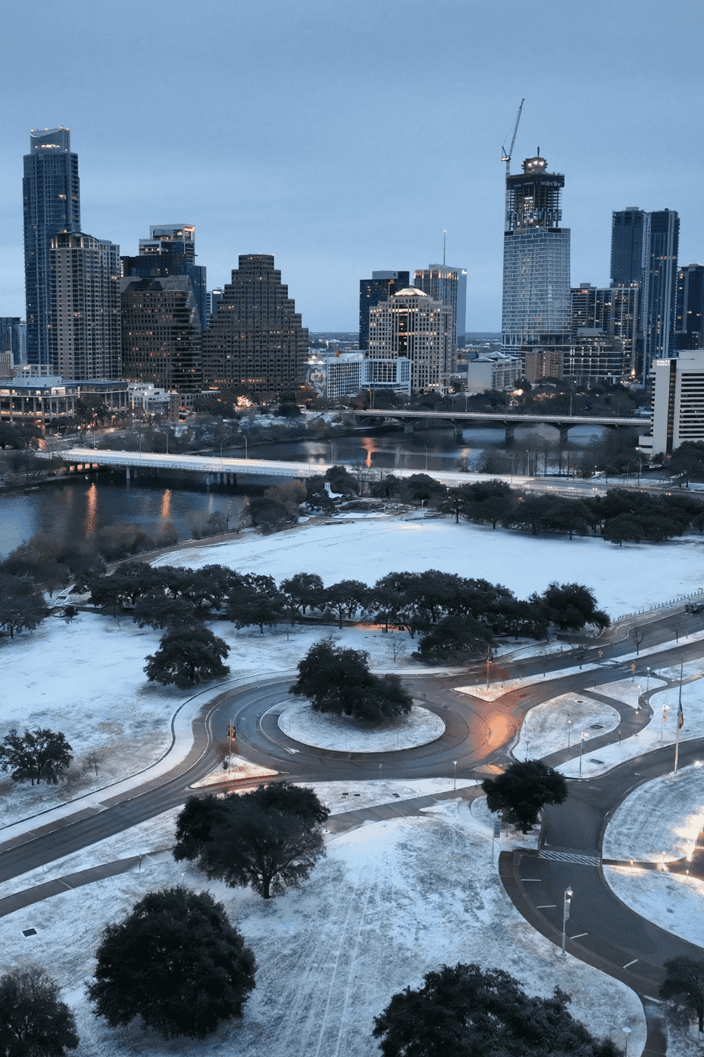 Snow-covered city park with modern downtown skyline in the background, showcasing urban nature and architecture.