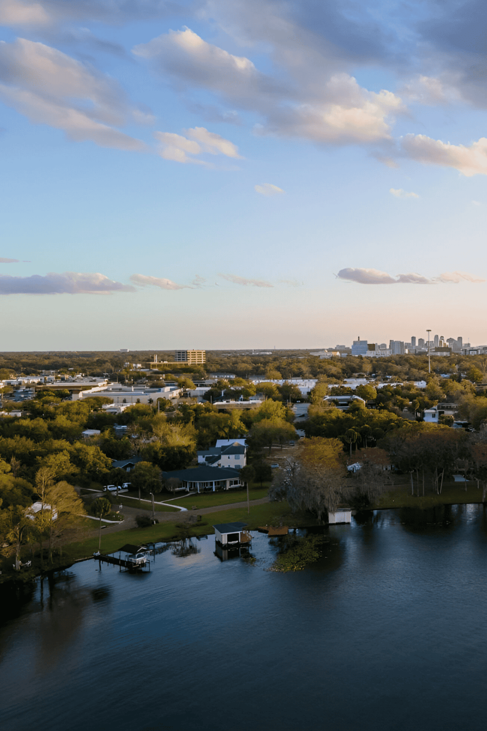 Backyard lake with houses and city skyline in distance, sunny sky with clouds, scenic outdoor view.