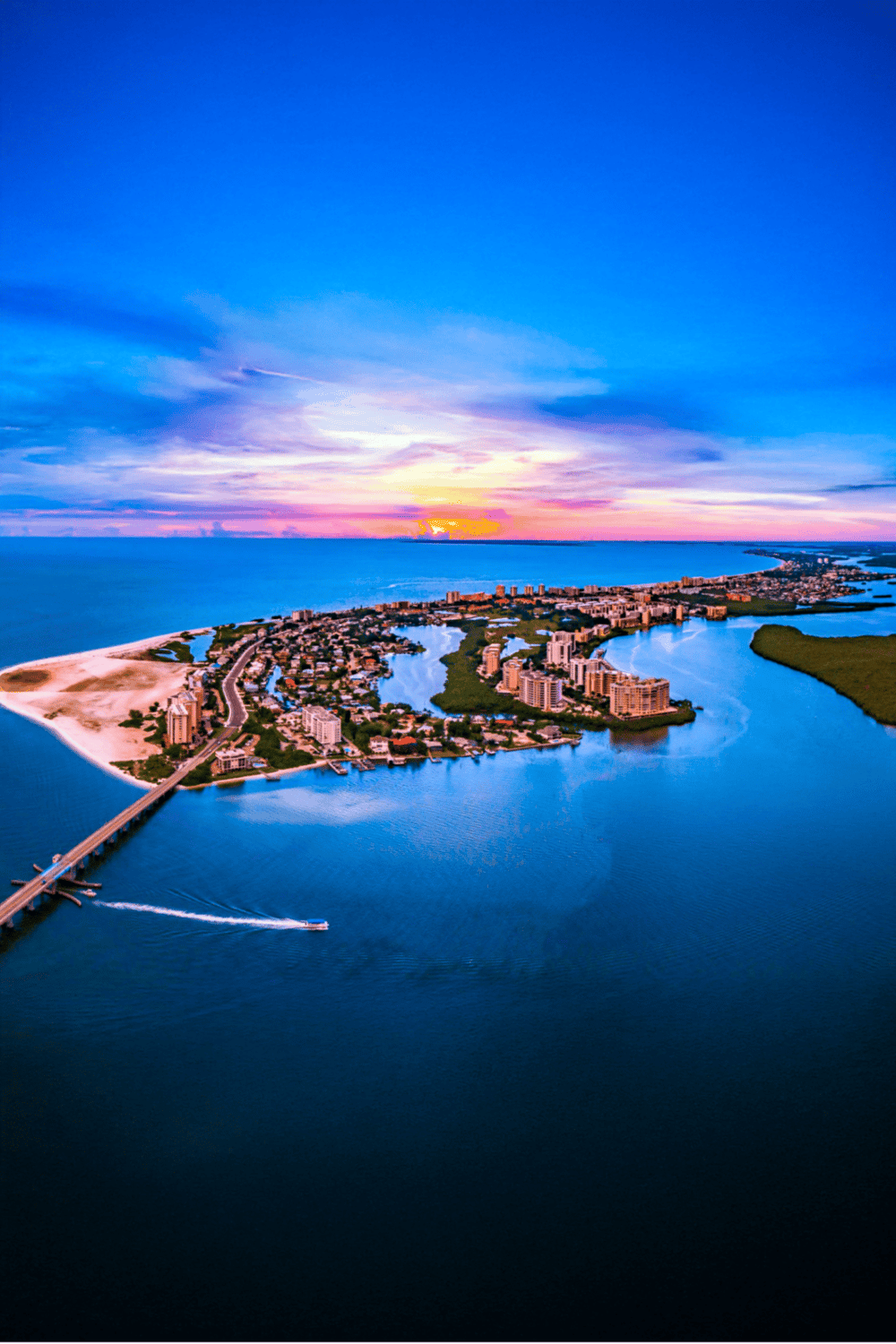 Aerial view of a coastal city at sunset with waterways and residential buildings, showcasing scenic Florida island scenery.
