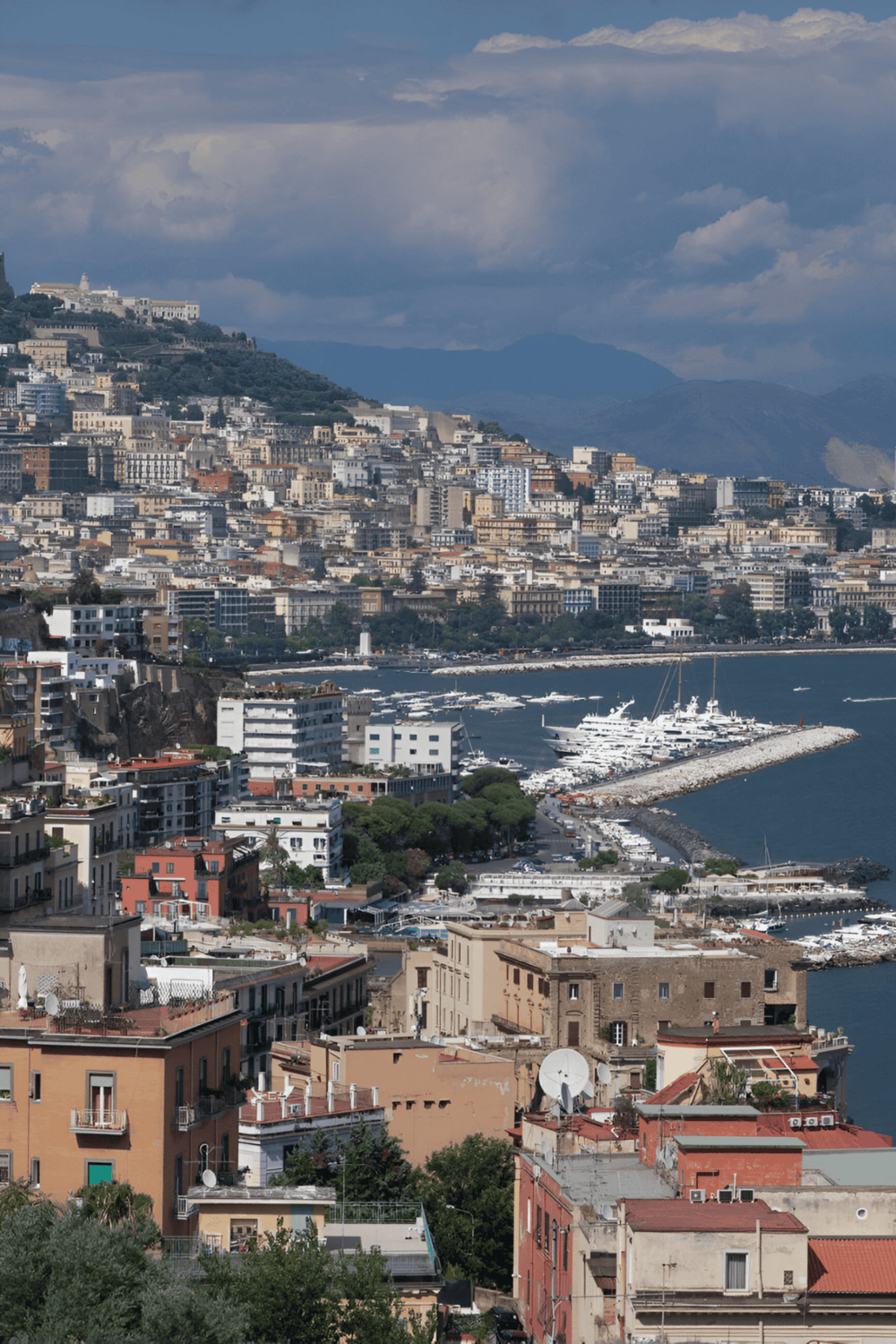 Coastal cityscape with marina, hillside buildings, and mountain backdrop in Italy, showcasing QuestForDirections services.