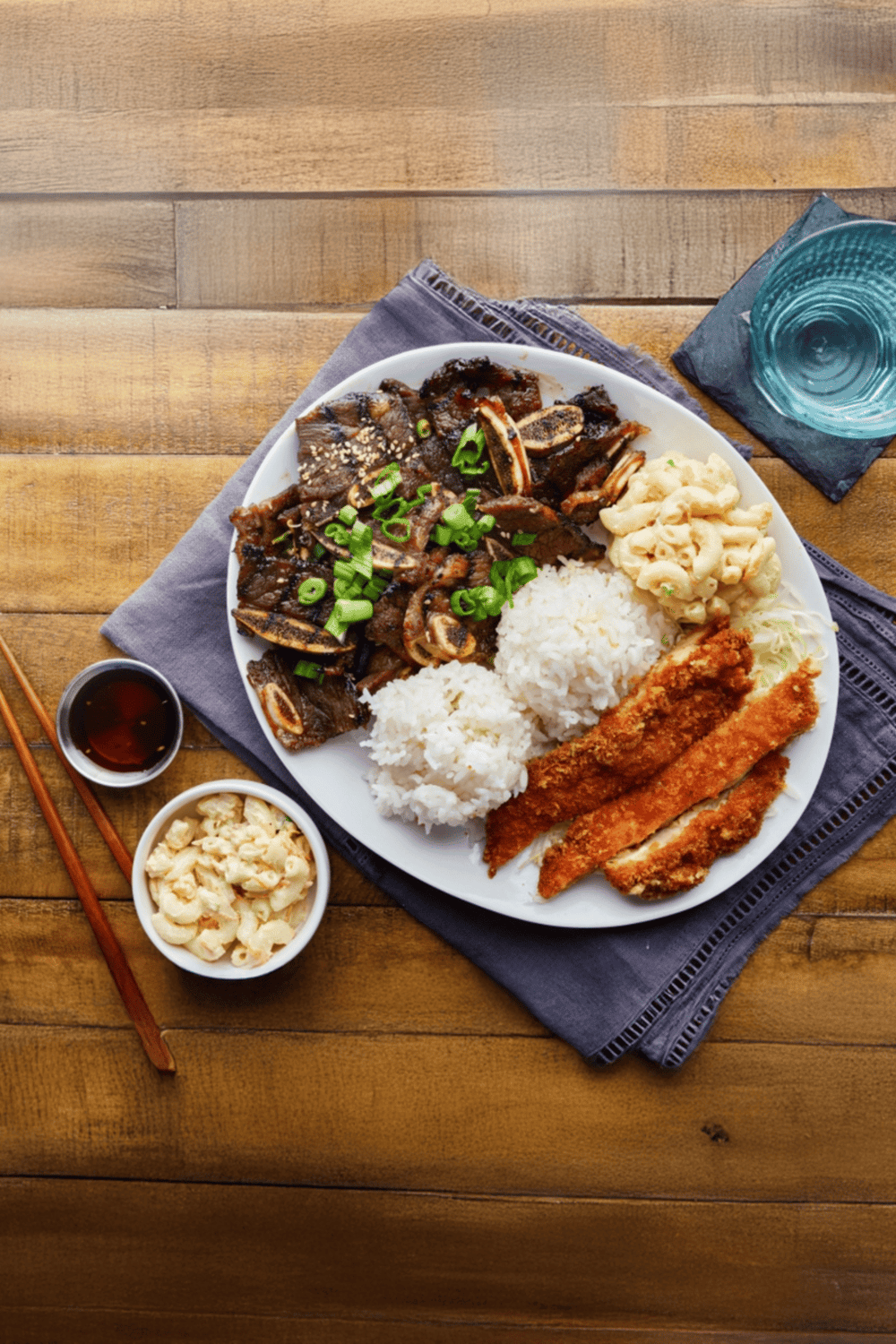 Authentic Asian cuisine plate with rice, beef, fried fish, and side dishes on wooden table.