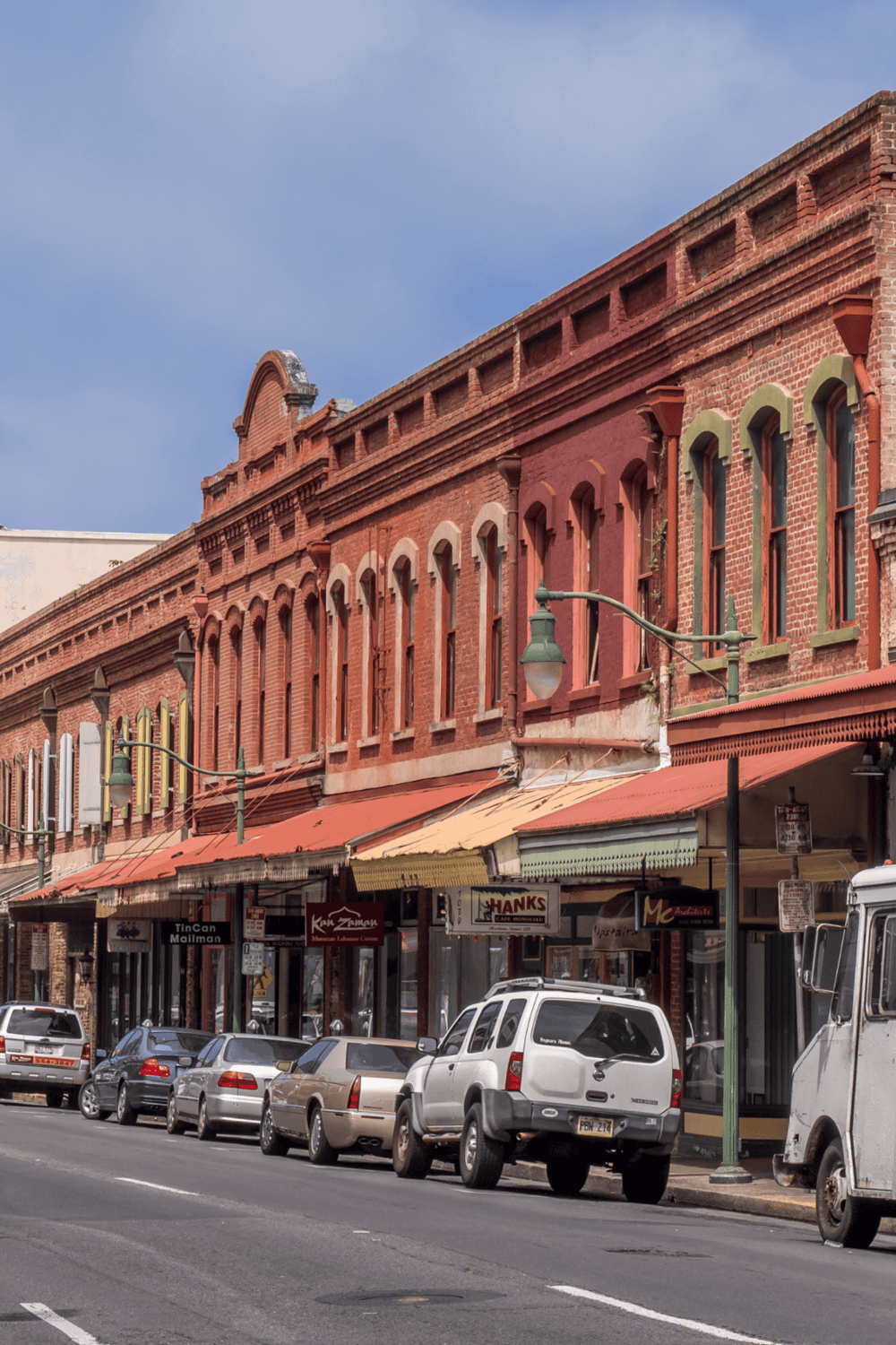 Colorful historic downtown storefronts, parked cars, and brick building architecture in a lively city scene.