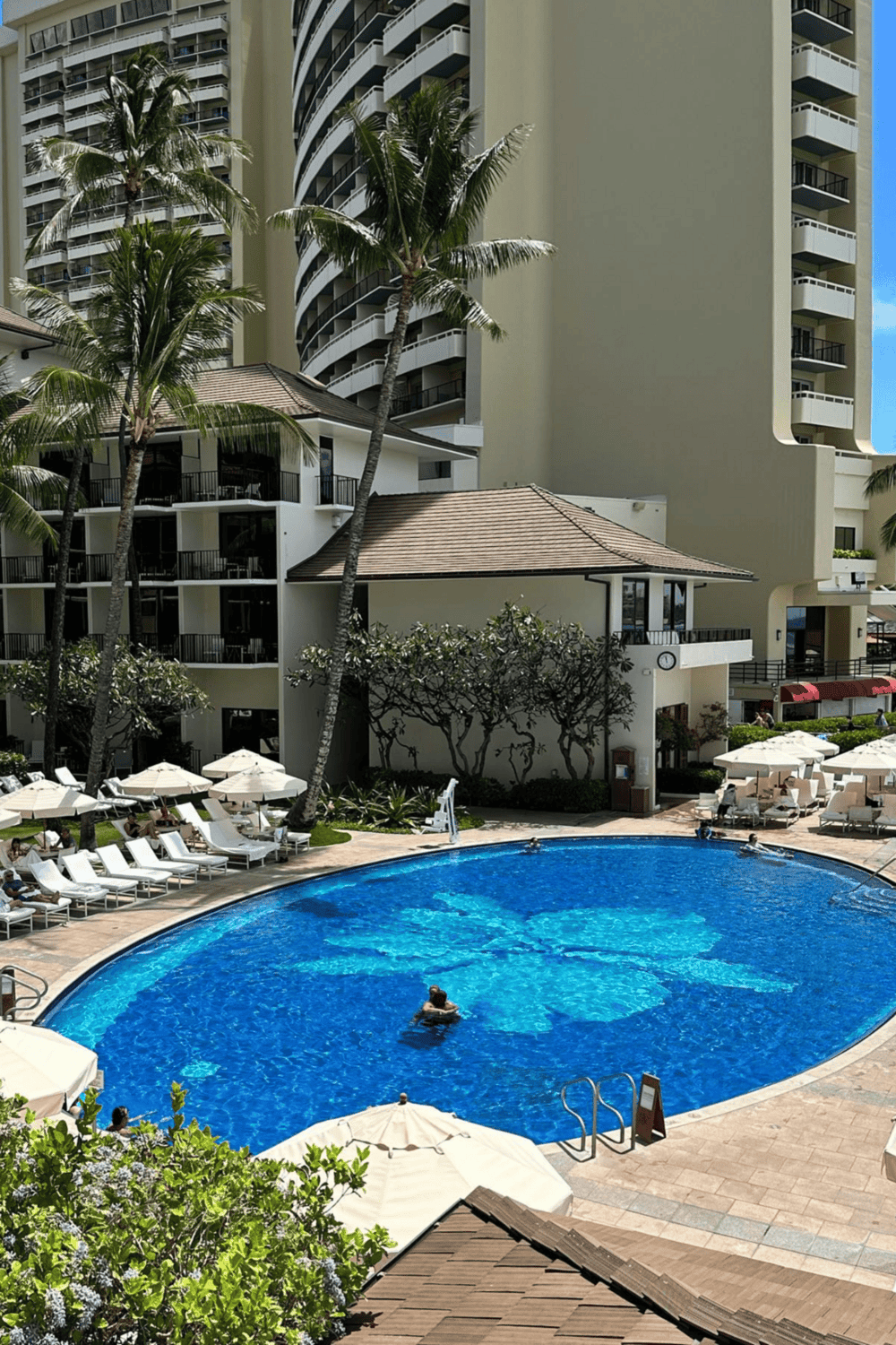 Luxury hotel swimming pool with sun loungers and palm trees in a tropical resort.