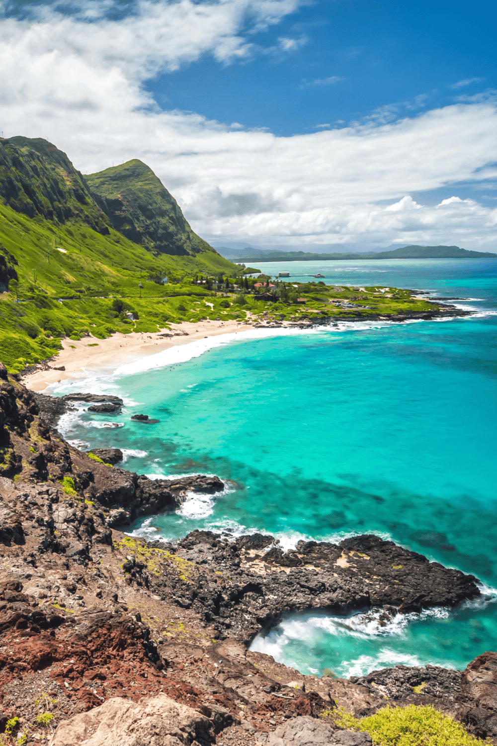 Vibrant tropical coastline with lush green cliffs and turquoise ocean waves.