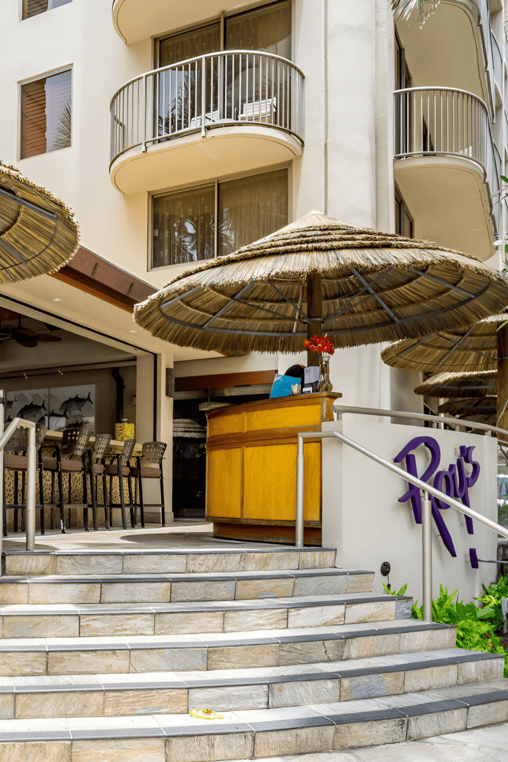 Relaxed outdoor bar with tropical umbrellas and hotel balconies in the background.