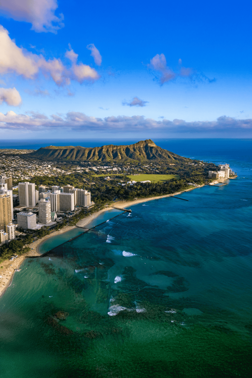 Vibrant aerial view of Diamond Head, Waikiki shoreline, and Honolulu skyline on a clear sunny day.