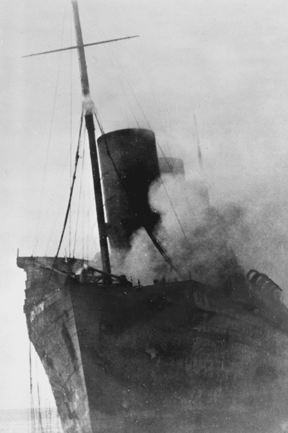 Smoke rising from ship fire during maritime disaster, historic black-and-white photograph of Titanic sinking.