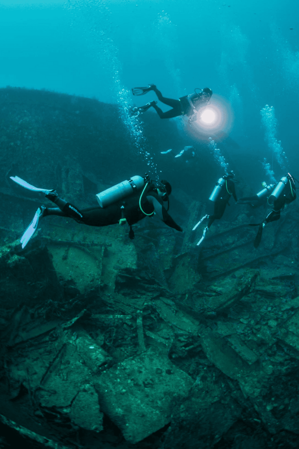 Diving explorers exploring underwater shipwreck with scuba gear and underwater flashlight.