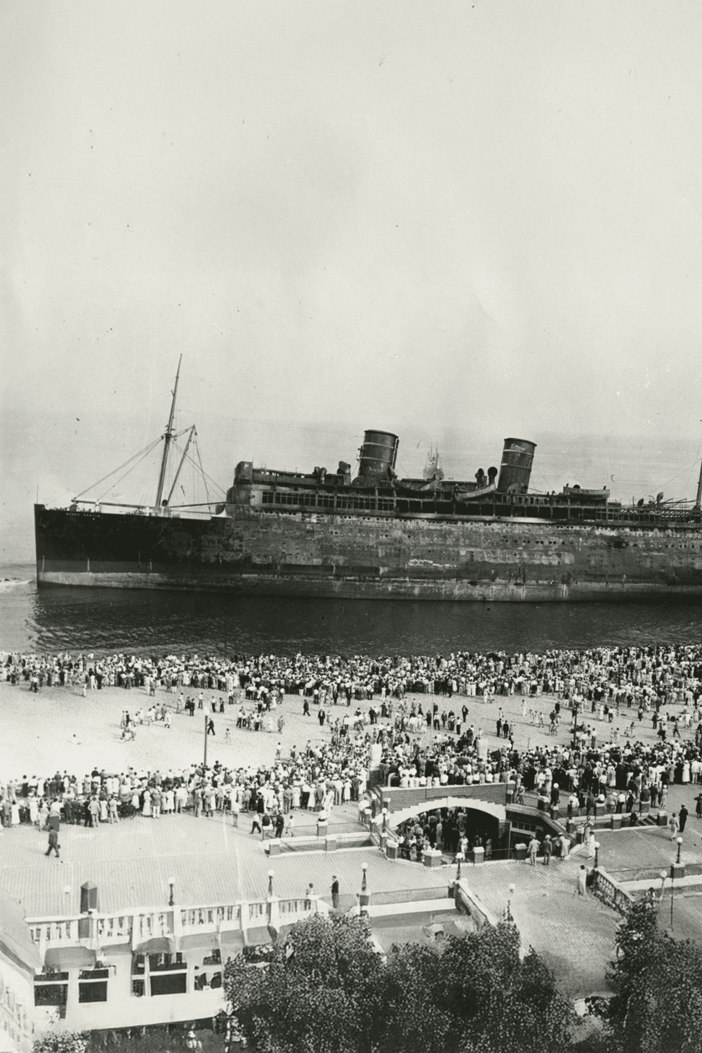 Old shipwreck surrounded by a crowd of people on the shore, historical maritime disaster, Titanic sinking, legacy of unmatched tragedy.