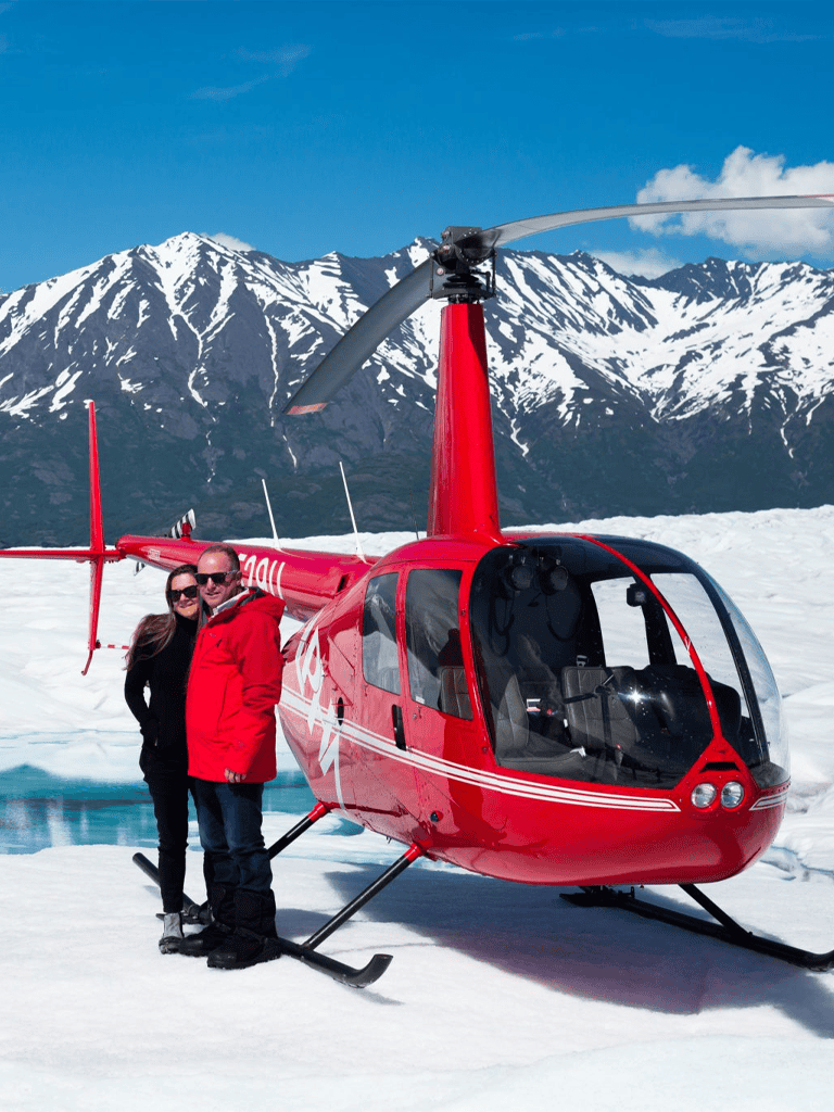 Aerial helicopter tour over snowy mountain landscape with couple in red and black jackets.