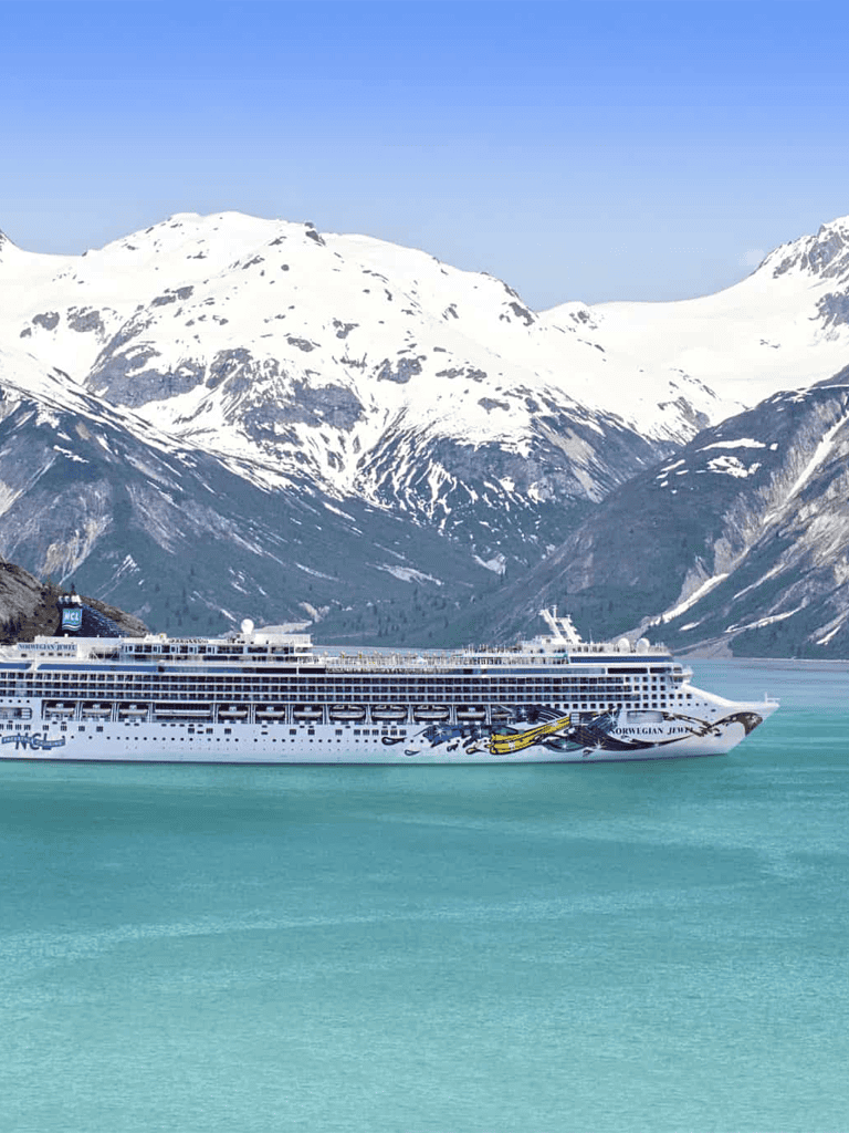 Cruise ship sailing with snowy mountain backdrop in scenic fjord.