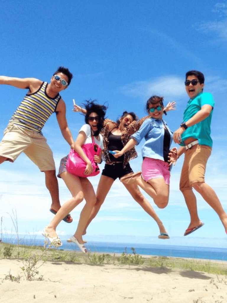 Vibrant group of friends jumping on a beach vacation, enjoying sunny weather and scenic ocean views.