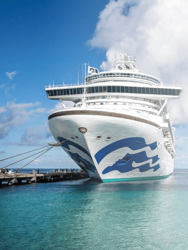 Luxury cruise ship docked at port with clear blue sky and turquoise water.