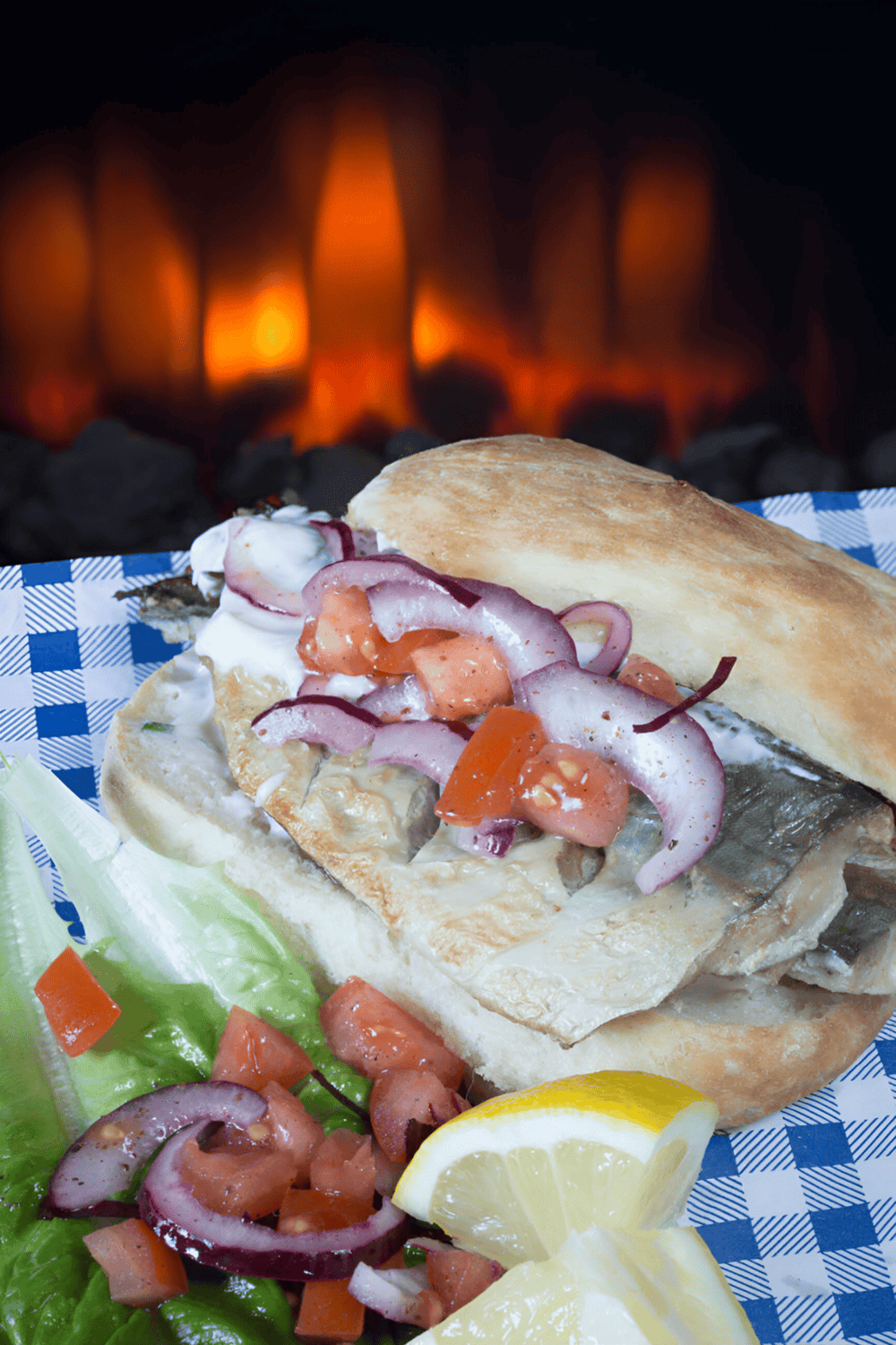 Fresh grilled fish sandwich with vegetables and lemon, served in a cozy restaurant setting.