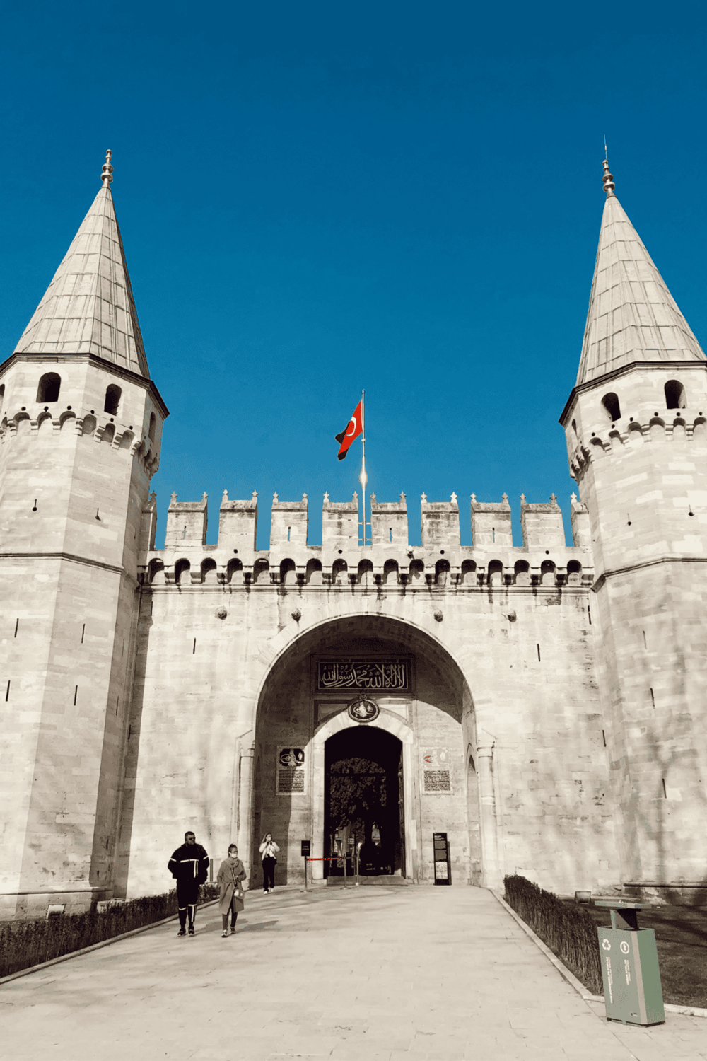 Ancient castle entrance with two towers and Turkish flag under clear blue sky.