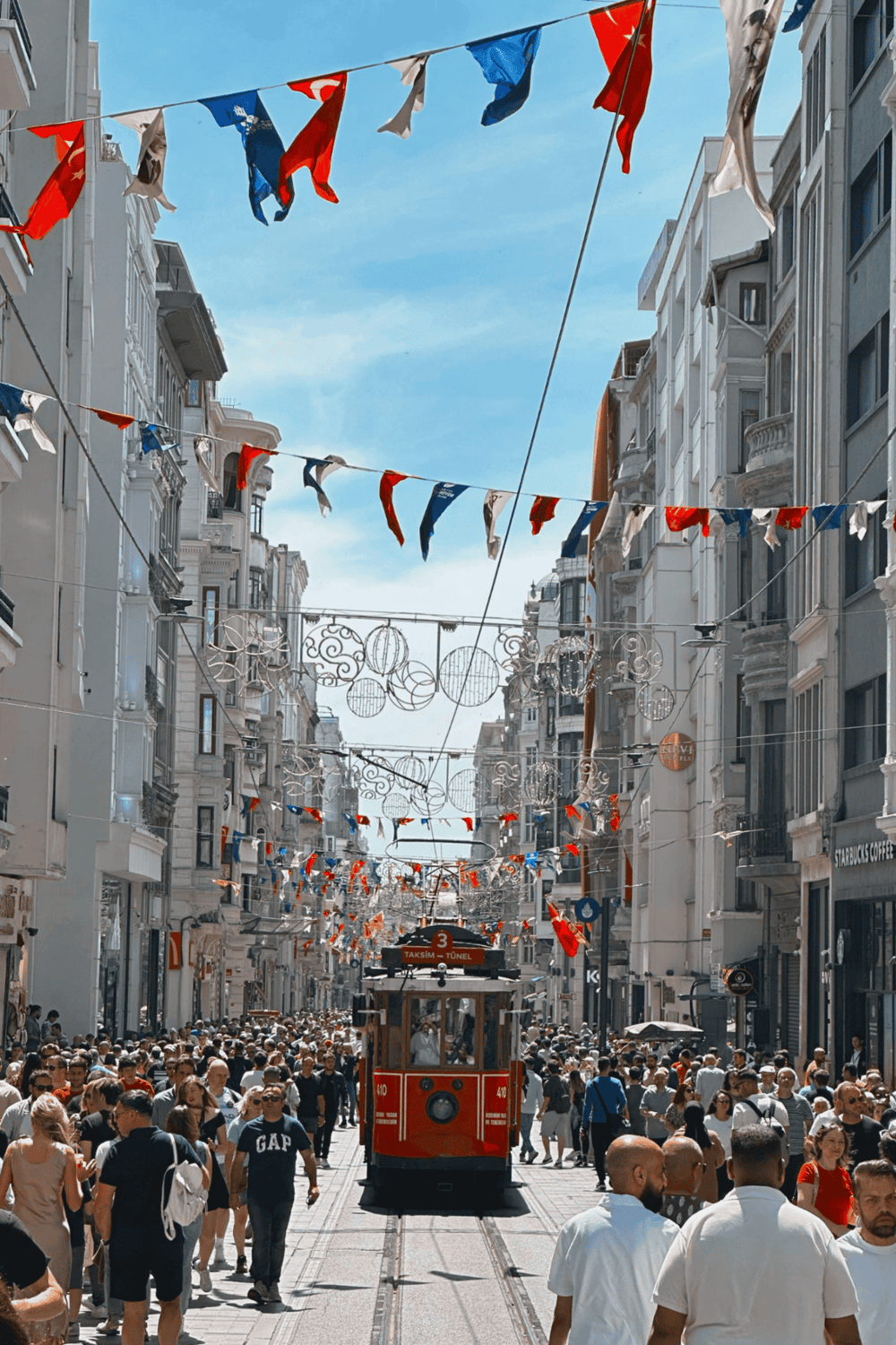 Crowded street in Istanbul with colorful flags and historic tram, lively cityscape, popular tourist destination.