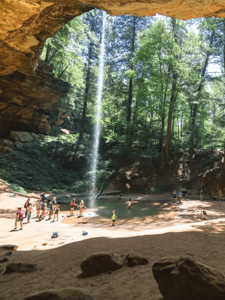 Majestic waterfall in lush forest cave with hikers and nature enthusiasts exploring scenic beauty.