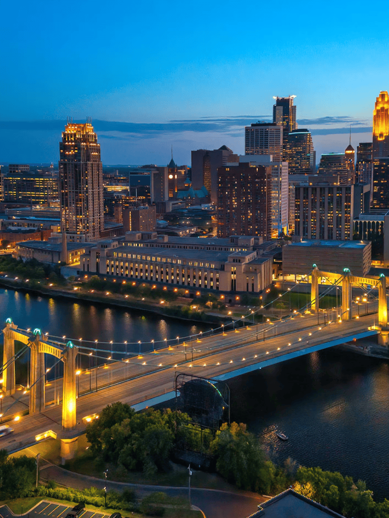 City skyline with illuminated skyscrapers and bridge over water at dusk, guiding urban navigation.