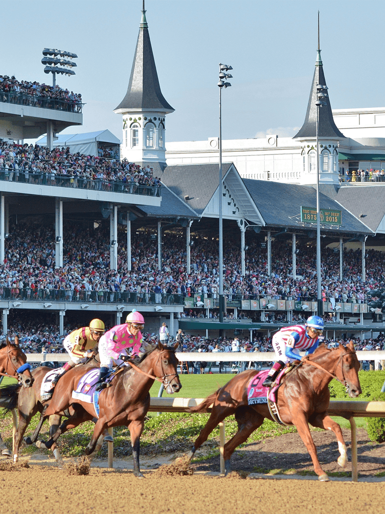Exciting horse race at a historic racetrack with cheering crowd and grandstand in the background.
