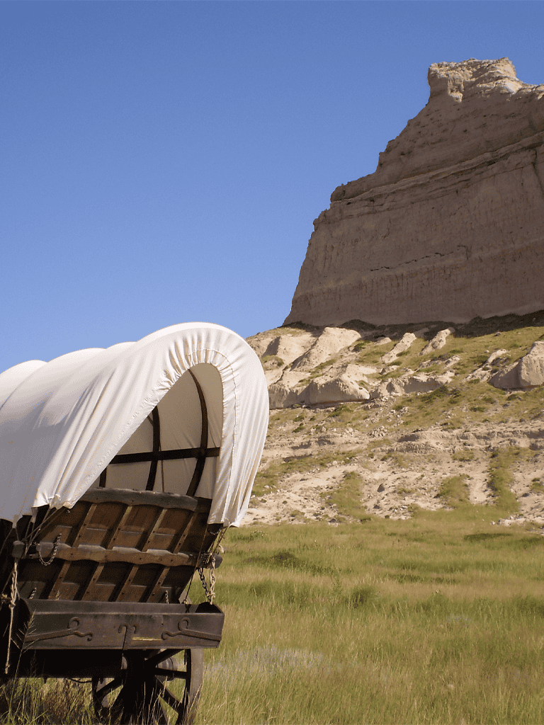 Covered wagon in a scenic landscape with cliffs and clear blue sky, representing adventure and travel.