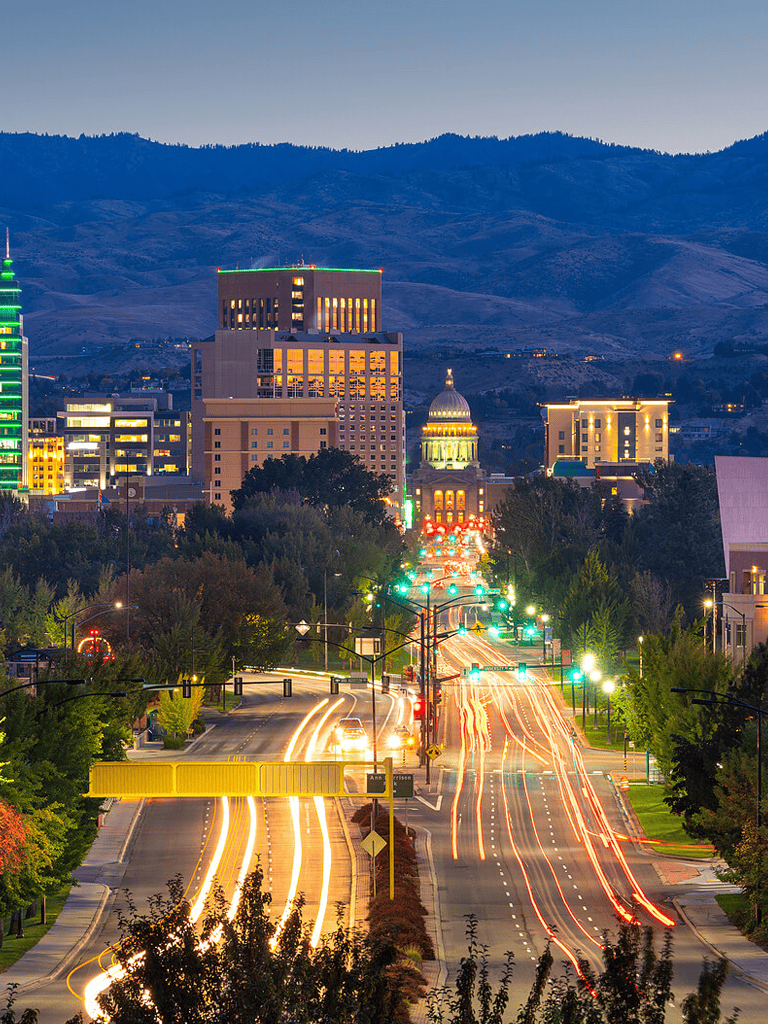 Colorful cityscape of Boise Idaho with vibrant nightlife and mountain backdrop, highlighting downtown and traffic at dusk.