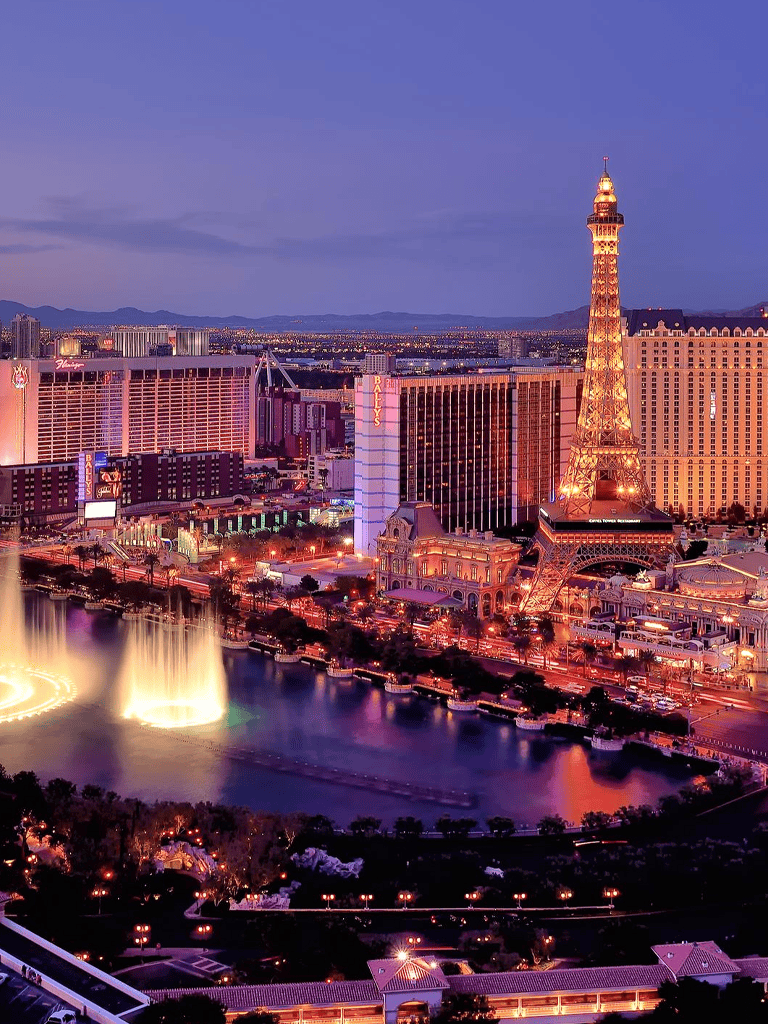 Brightly lit Las Vegas Strip with Eiffel Tower replica and Bellagio Fountain at dusk, showcasing iconic nightlife and entertainment.