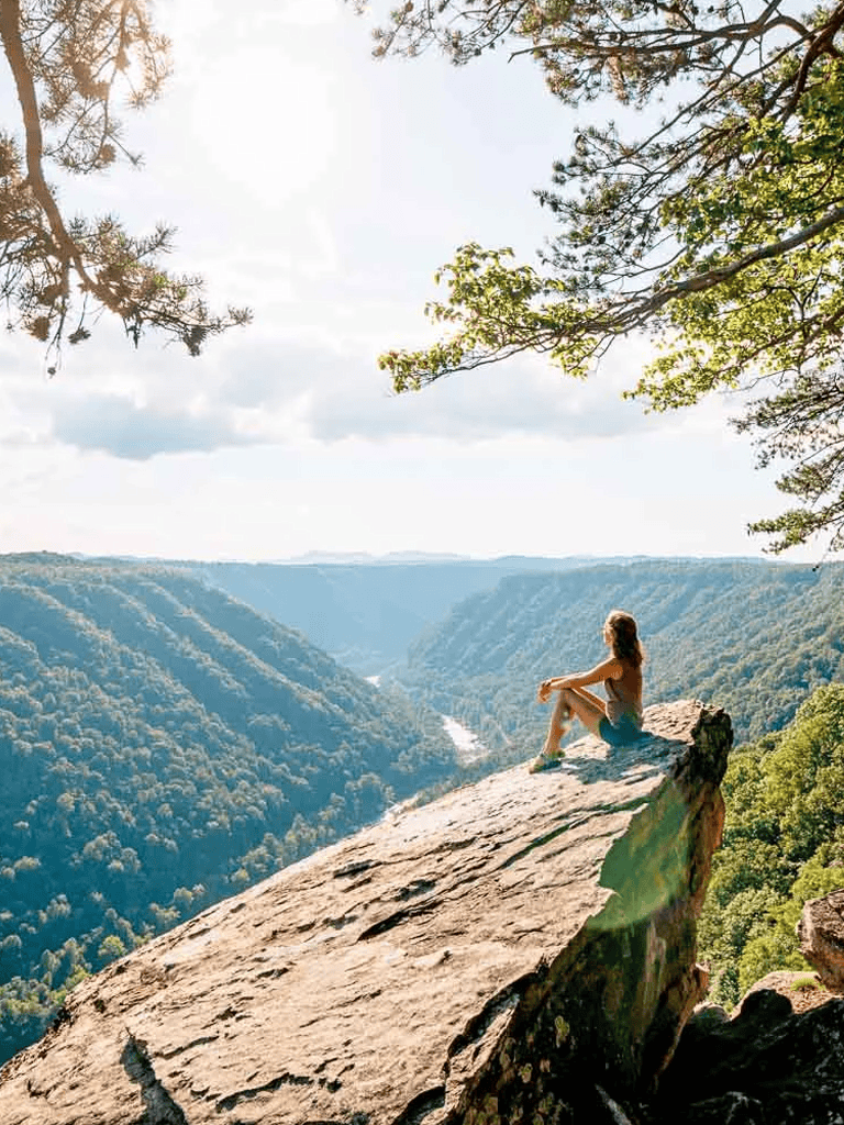 Serene woman sitting on cliff edge overlooking lush canyon landscape at sunset.