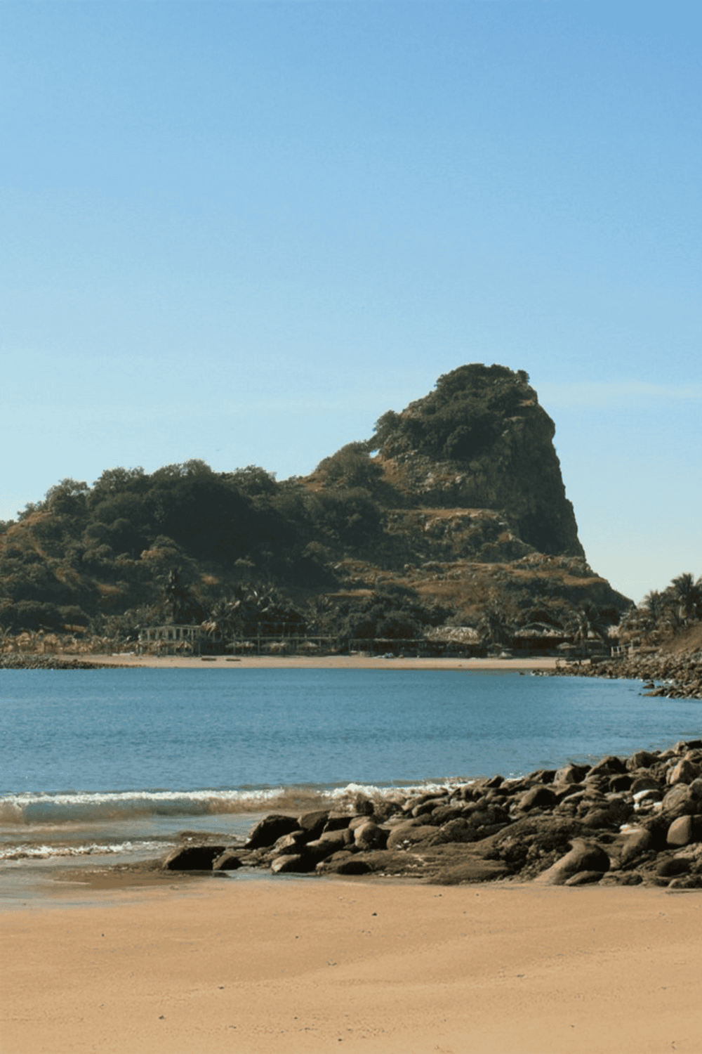 Seaside beach with rocky shoreline, lush green hill and scenic mountain in the background, ideal for travel and adventure enthusiasts.