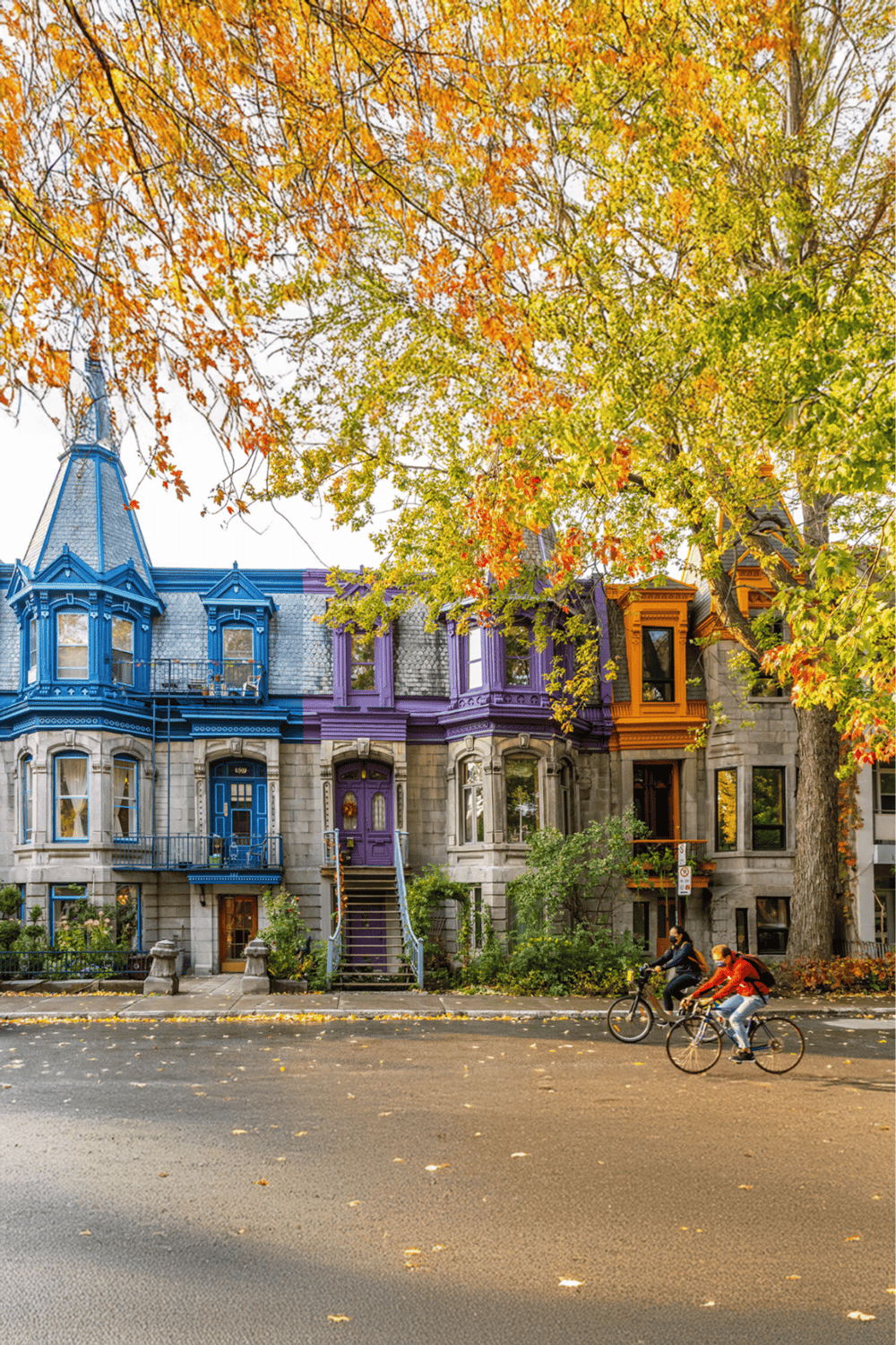 Colorful Victorian houses in Vancouver, BC, with autumn foliage and cyclists riding along the street.