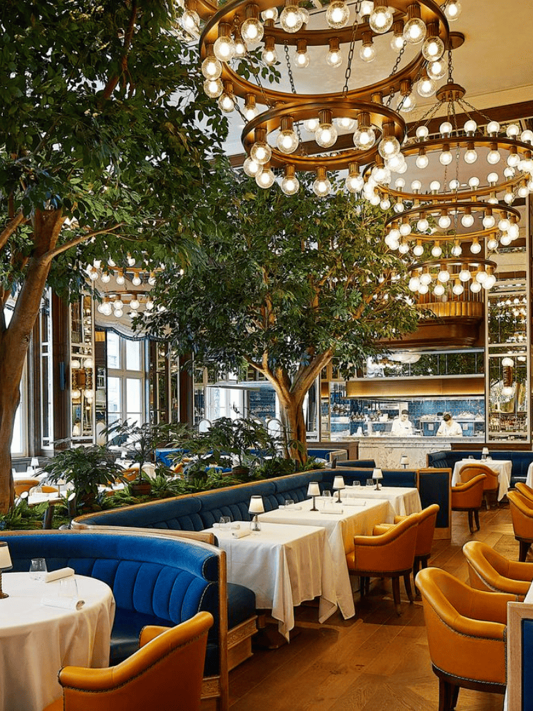 Elegant restaurant interior with lush greenery, warm lighting, and stylish seating arrangements.