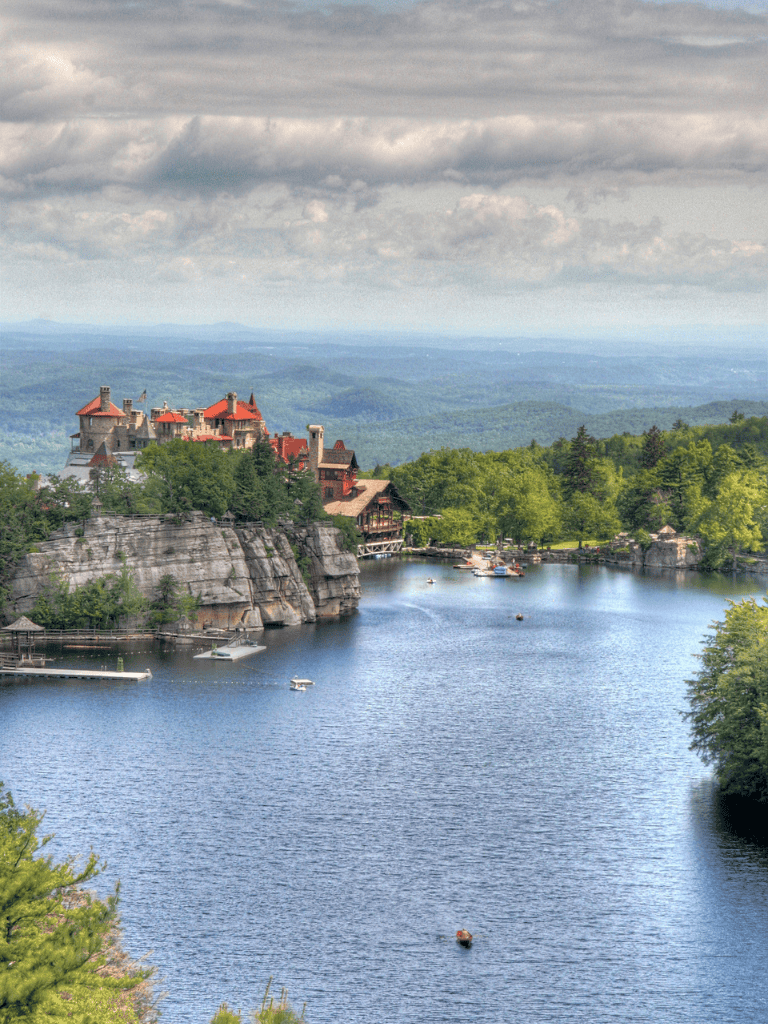 Elegant castle on a hillside overlooking a peaceful lake surrounded by lush greenery.