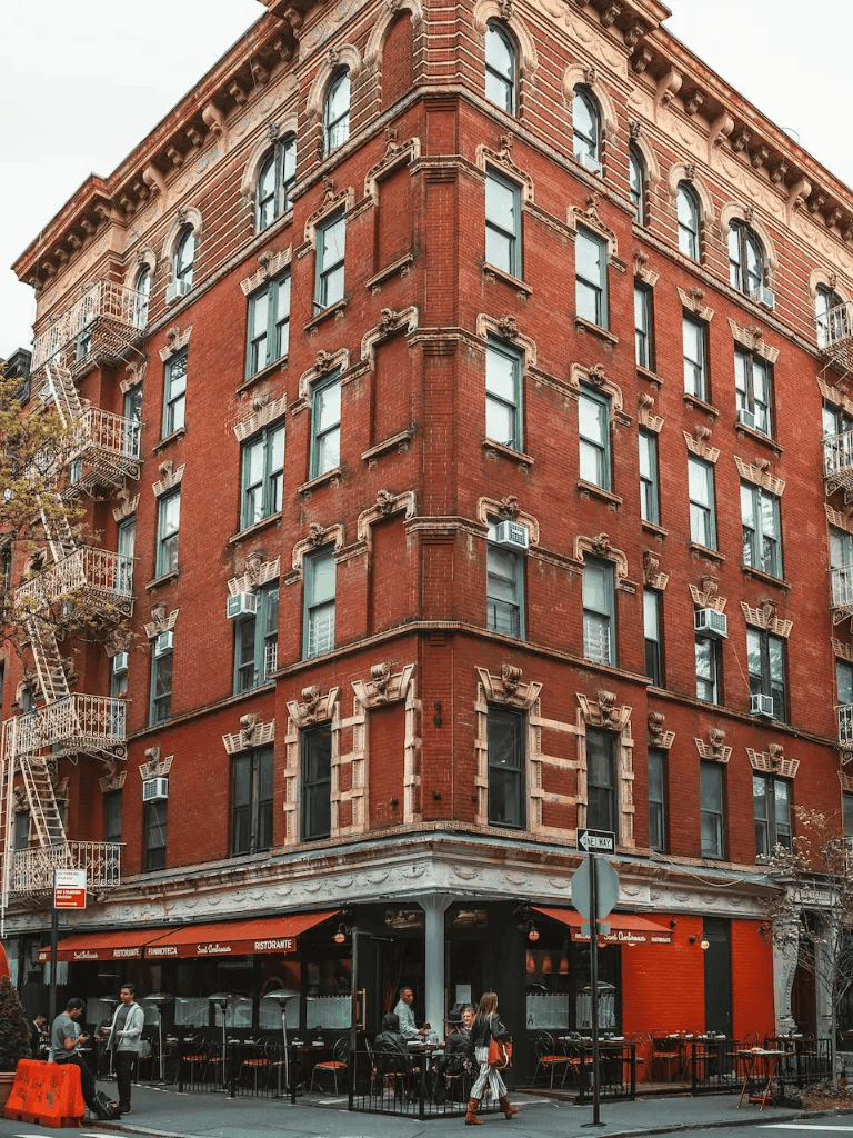 Old brick apartment building with ground-level restaurant and people walking on the street.