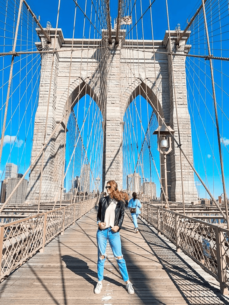 Vibrant woman on Brooklyn Bridge with NYC skyline, iconic suspension bridge, travel photography, urban sightseeing, QuestForDirections.