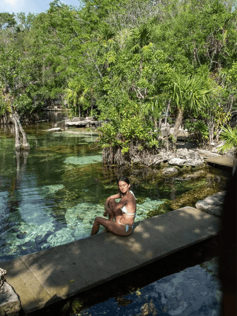 Serene woman relaxing by tropical spring surrounded by lush greenery and clear water.