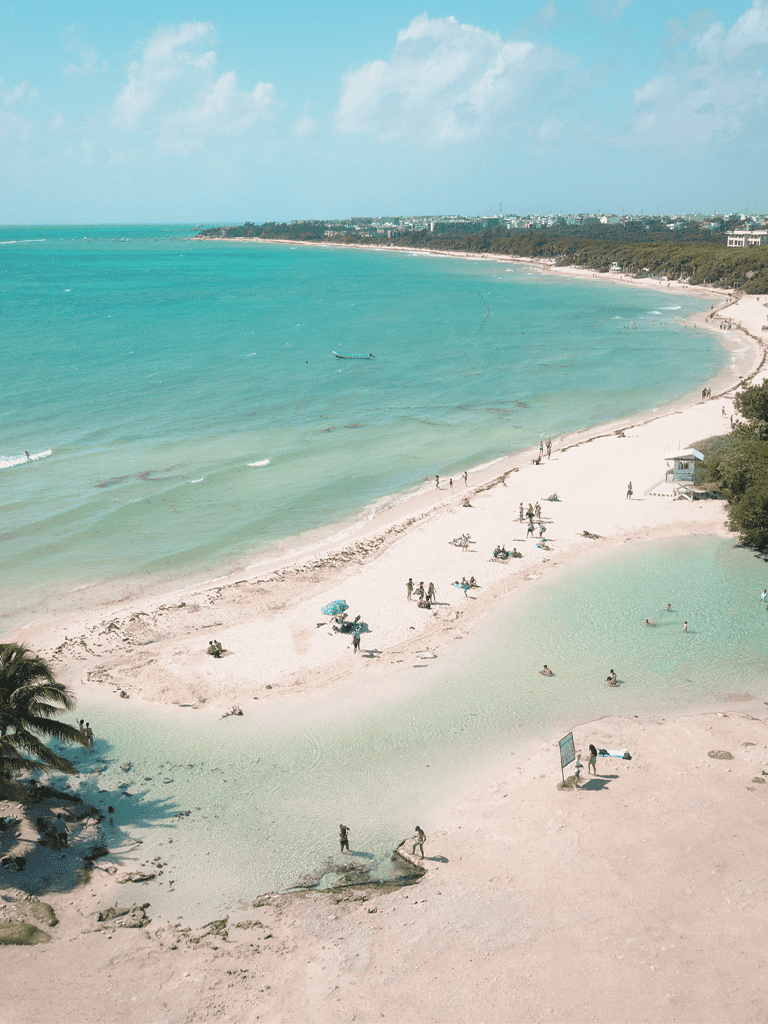 Turquoise beach with clear waters and people enjoying seaside activities.