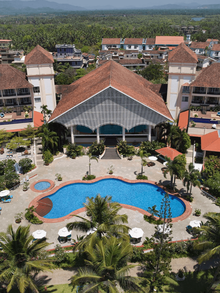 Lush tropical resort with swimming pool, palm trees, and modern buildings in a scenic location.