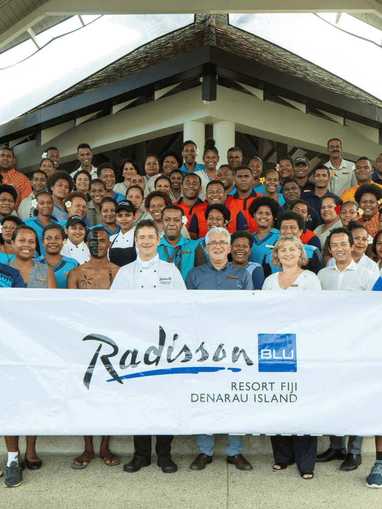 Diverse group of hotel staff and guests at Radisson Blu Resort Fiji on Denarau Island, promoting hospitality services.