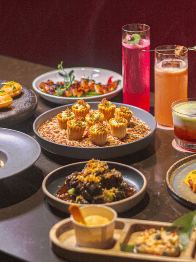Spicy Indian appetizers with colorful drinks on a dark table.