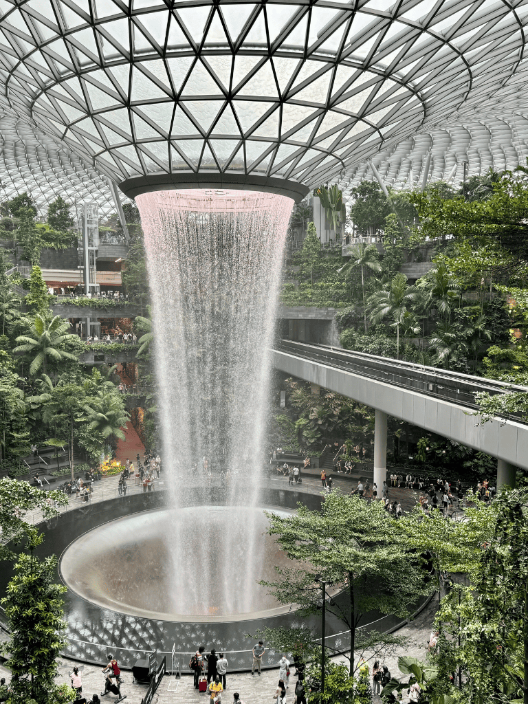 Indoor waterfall at Jewel Changi Airport, Singapore, lush greenery and modern architecture.