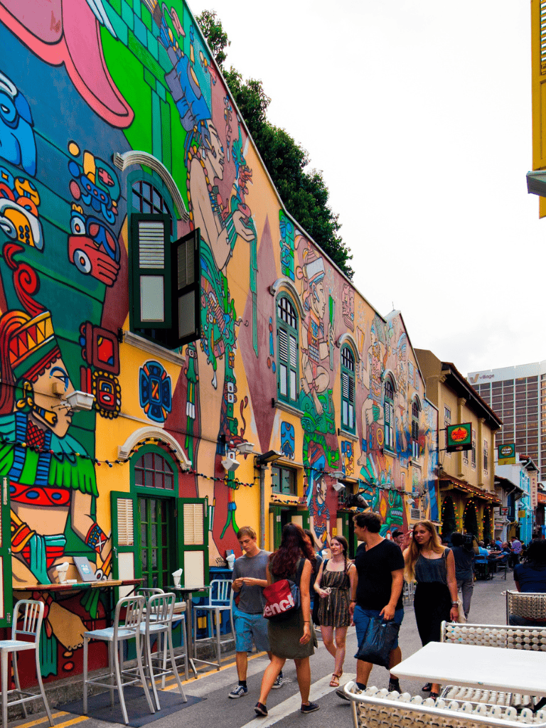 Vibrant alley with colorful mural art, outdoor seating, pedestrians, lively urban scene, artistic murals, street art, community atmosphere.
