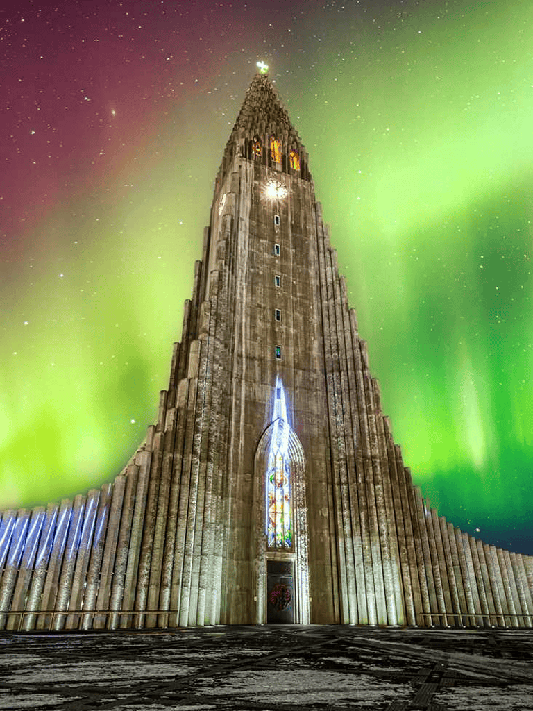 Majestic church tower illuminated under the aurora borealis with colorful northern lights in the background.