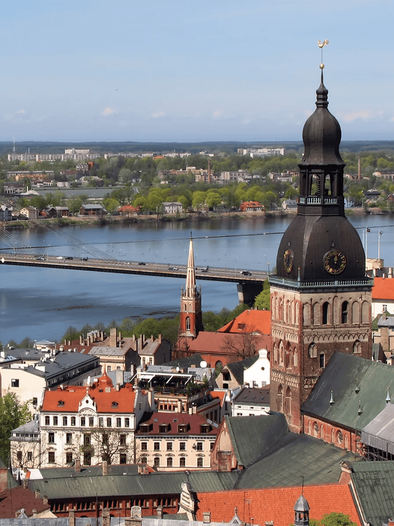 Historic church tower with cityscape and bridge over river in the background, scenic view of city architecture.